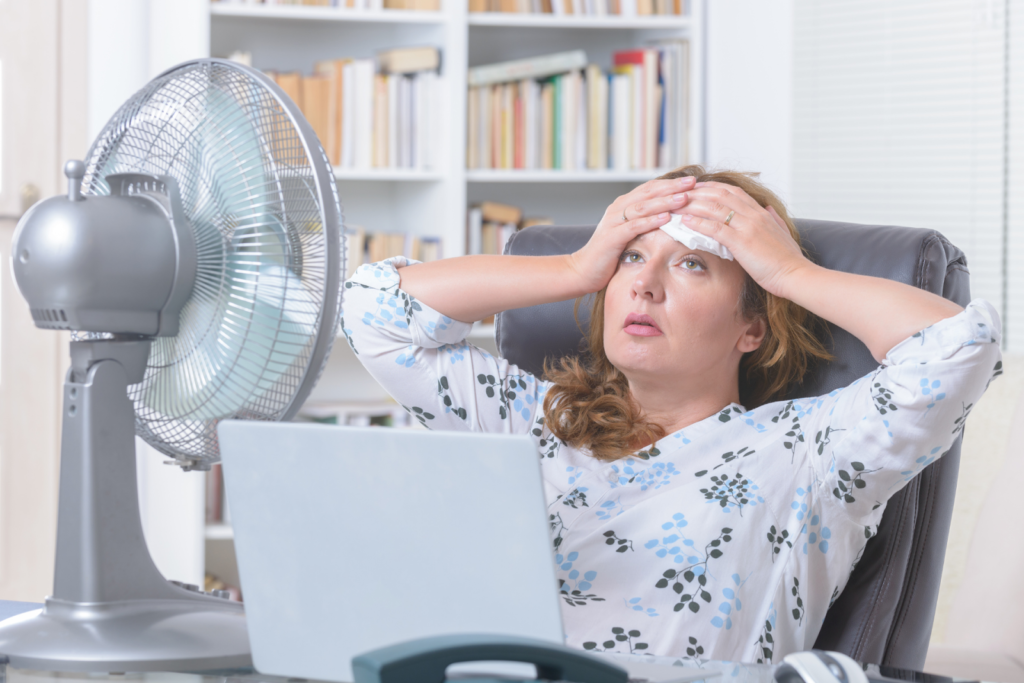 sweaty woman cooling down with fan because of broken ac